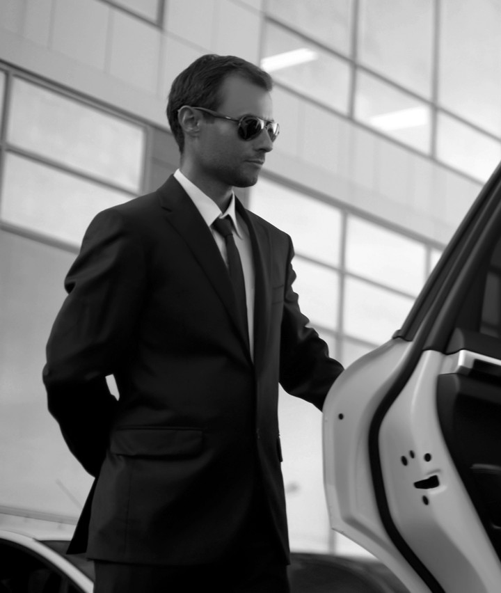 Guard in sunglasses holding open a car door